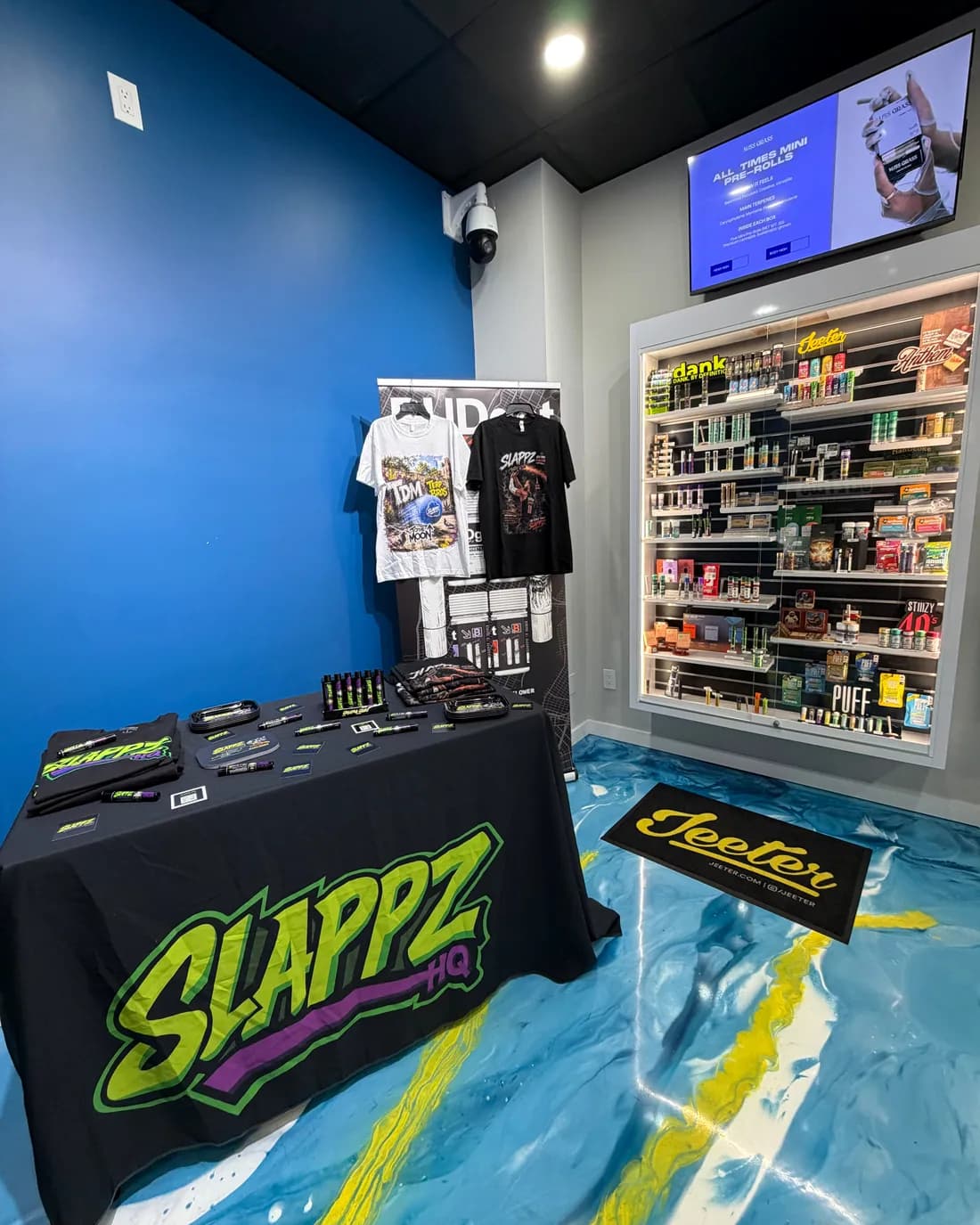 A SLAPPZ HQ branded table beside a stocked product wall in a licensed dispensary.